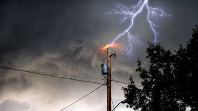 lightning bolt striking an electrical pole with trees nearby