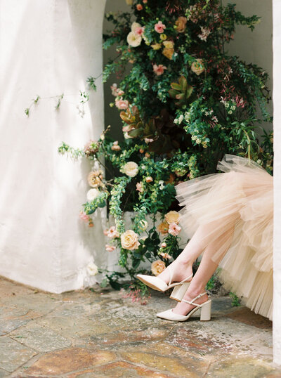 Cropped photograph of brides shoes and dress with surrounding florals at Korakia in Palm Springs