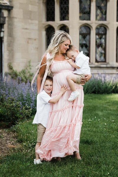 A woman holding a toddler and standing next to a young boy outdoors for maternity photography.