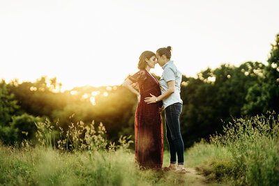 pregnant couple in long grass at sunset