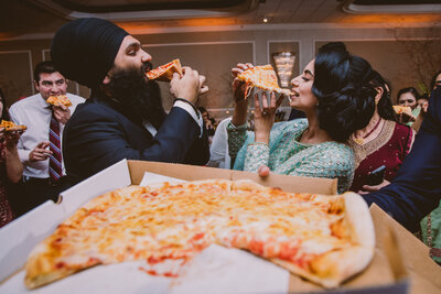 Sikh bride and groom taking a bite of pizza at their wedding reception