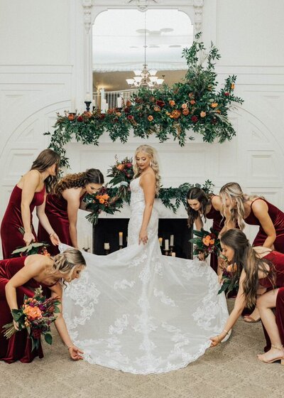 bridesmaids fixing bride's gown in front of fireplace
