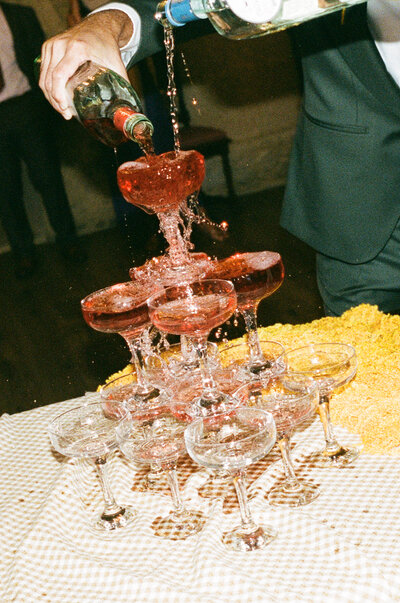 Film photo of bride and groom kissing and cheers-ing while sitting at head table during wedding reception