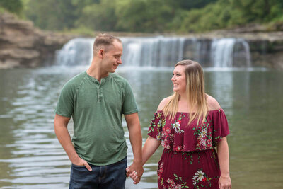 Engaged couple holds hands in front of waterfall