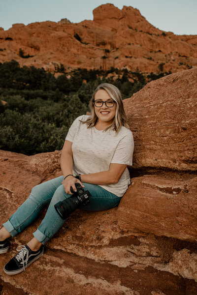 Kayla holding her camera, sitting on some red rocks at garden of the gods