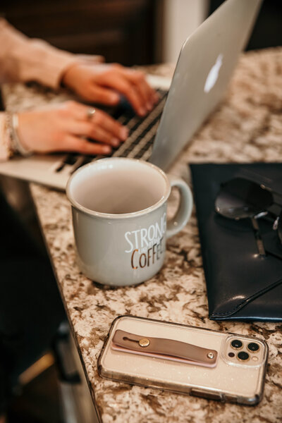 woman typing on laptop next to mug and cellphone