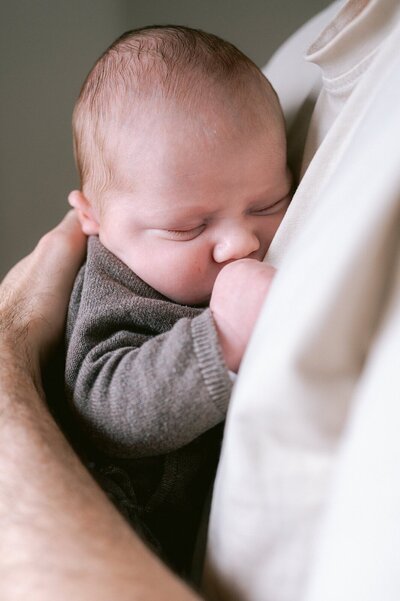 Newborn baby ligt tegen de borst van papa aan te slapen