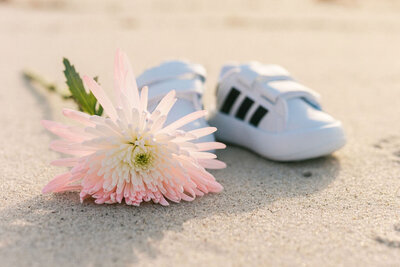 Baby sneakers and pink flower on the sand during a maternity session on Miami beach.