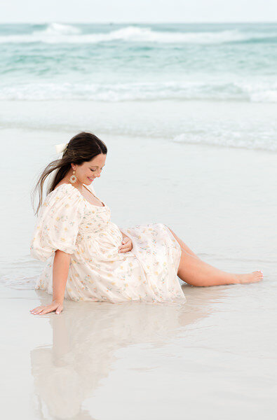 Expecting mother sitting peacefully on the shore in a floral dress during her maternity session by Andrea Krey Photography in Destin