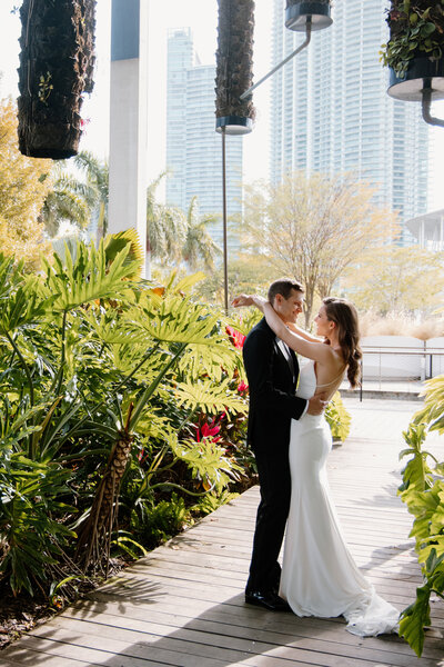 Outdoor portrait of a bride and groom embracing in a lush garden setting with Miami's skyline in the background, captured by Rodrigo Varela Photography. Elegant Miami wedding photography highlighting romantic moments in natural surroundings.