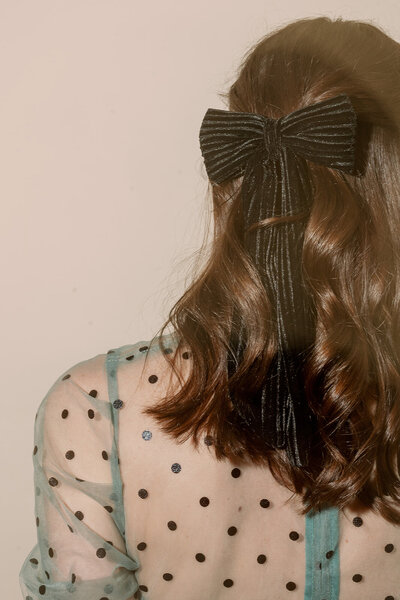 Back of a woman's head with brown hair wearing a black velvet hair bow