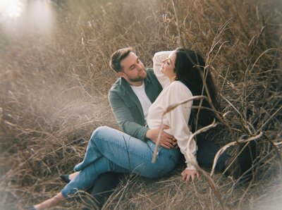 A romantic and intimate engagement session in the natural landscapes of Dallas-Fort Worth, featuring a couple nestled in tall golden grasses, sharing a quiet moment.