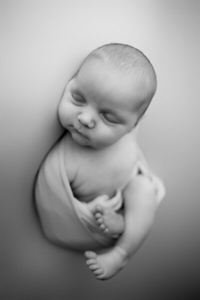 Black and white image of newborn with eyes open and parents with hands on them