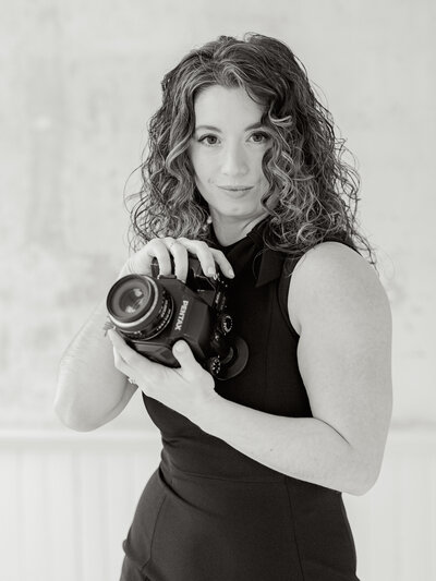 Black and white headshot of Lauren Baker holding up her camera