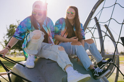 Two girls in tie dye jerseys sit on a playground