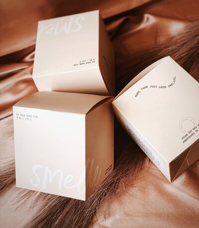 Smelle candle company box packaging laying on smooth fabric