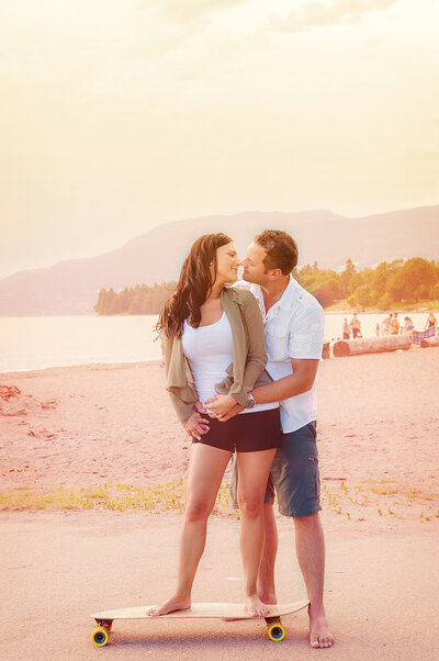 Couple on a long board at a Vancouver beach just about to kiss at sunset.