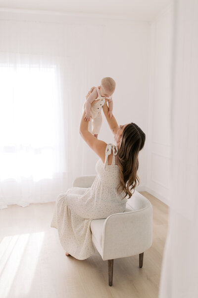 A mother lovingly holds her baby boy up in the air while smiling at each other.