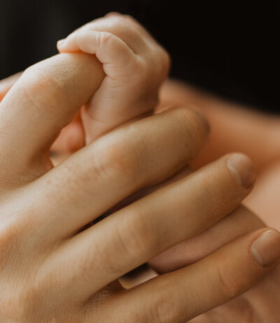A newborn holding her father's finger.