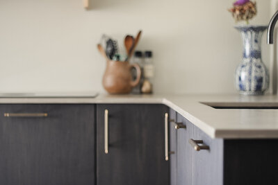 Een stijlvolle keuken met donkere houten kastdeuren, strakke koperen handgrepen en warme accessoires, ontworpen door LOOSZ.