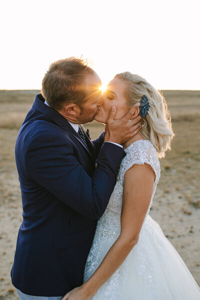 Candid moment of bride and groom sharing a sunset kiss on the salt pans, groom’s hands gently cupping her face.
