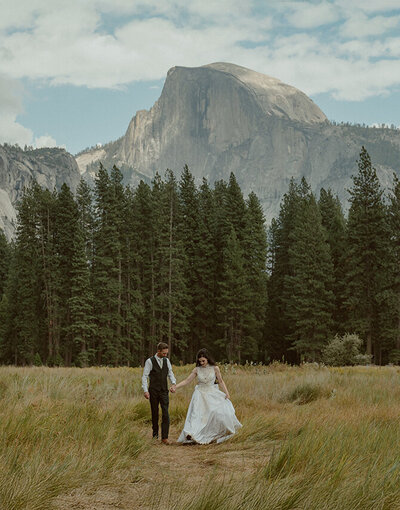 bride and groom walking in cooks meadow with view of half dome