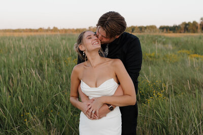 A person hugging their partner from behind as they kiss their cheek 