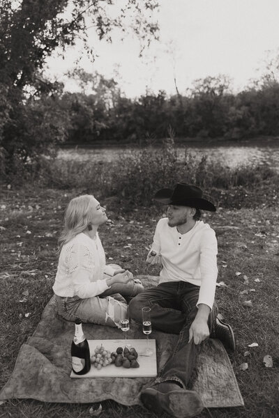 Couple sits on a picnic blanket with an assortment of foods