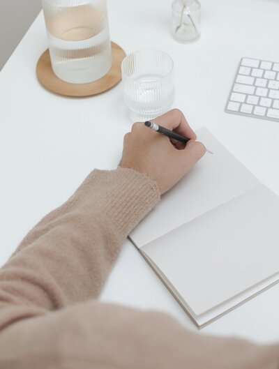 Person journaling in a blank notebook beside a keyboard and glass of water, symbolizing self-reflection, EMDR resourcing, and inner work in therapy with Jessie Withers, California