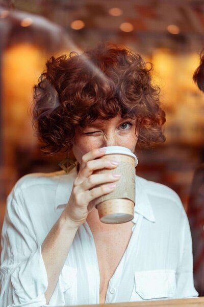 A woman with a content smile, drinking coffee from a cup, capturing a serene moment of indulgence.