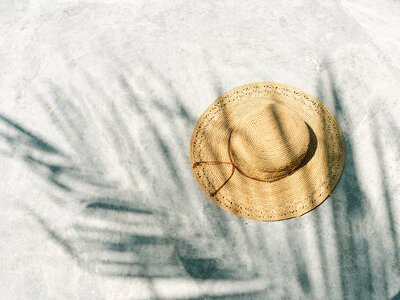 Straw hat laying on the ground with palm tree shadow over ti