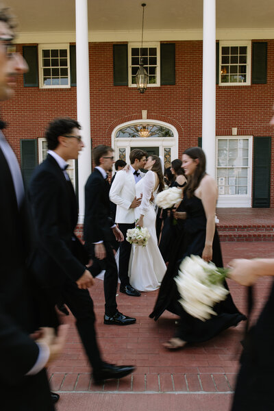 Bride and groom kissing while wedding party walks around them.