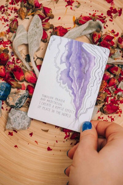 A hand holding an oracle card with a spiritual message, surrounded by dried flowers and crystals, symbolizing meditation, mindfulness, and intuitive guidance.