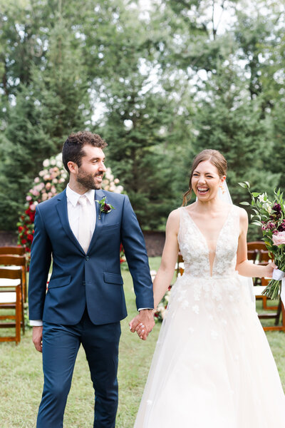 A young couple embraces on their wedding day. The groom looks at the bride who is looking into the camera. She's wear soft pink lipstick and natural eye makeup