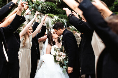 Man and woman kissing while bridal party surrounds them making an arch