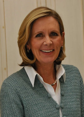 Elegant woman with short blonde hair smiling in a formal headshot with a neutral background.