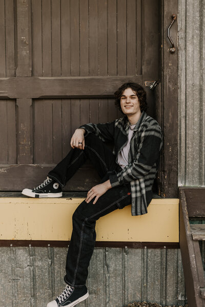 boy wearing plaid jacket sitting by garage doors