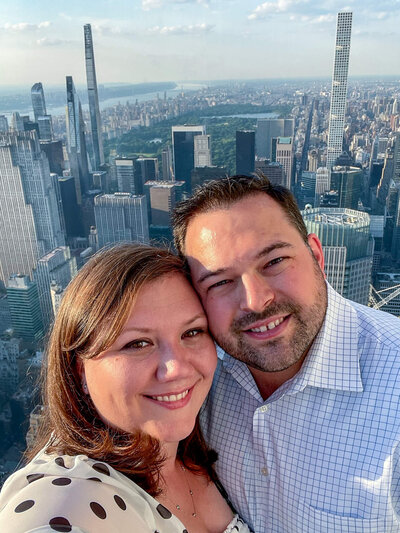 a couple smiling with their foreheads touching with a view of New York City skyline in the background at the top of SUMMIT One Vanderbilt in NYC