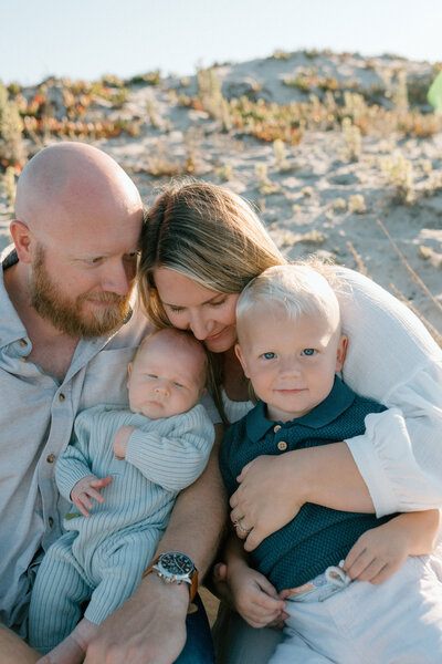 Molly, a San Diego photographer, standing on the beach with her partner and their baby, smiling at the camera during a family portrait session