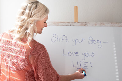 woman writing the phrase "shift your story, love your life" on a whiteboard