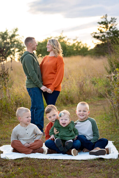 Four children sitting on a blanket in front of their parents smiling at each other during their Haymarket family photo session,