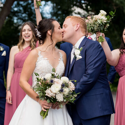 bride and groom kissing while their bridal party cheers behind them taken by Ottawa wedding photographer JEMMAN Photography at The Marshes wedding venue