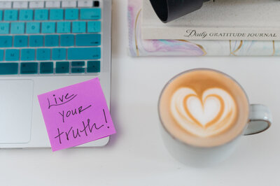 A flatlay branding image of a laptop with a sticky note that says Live Your Truth, a notebook, gratitude journal, and a cappuccino with heart shaped foam design.