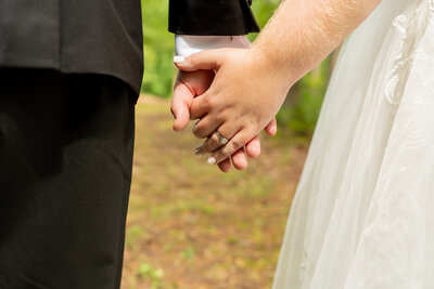 A close up of a bride and groom holding hands.