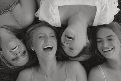 A black and white photo of 4 girls laying on the ground with their heads in a line and laughing together in Northeast, TN. 