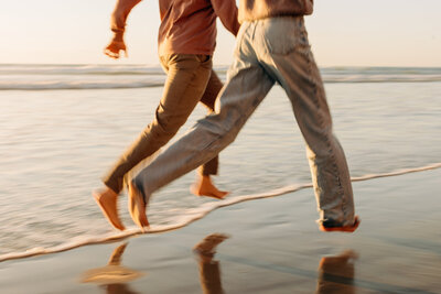 blurry legs of a couple running along the shore line of a san diego beach at golden hour