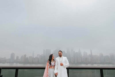 South Asian couple standing on rooftop overlooking New York City Skyline.