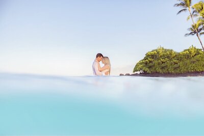 couples photoshoot in hawaii featuring husband and wife kissing in the water