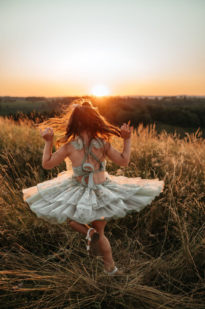 Young girl in a ruffled tulle dress twirling in the sunset. 