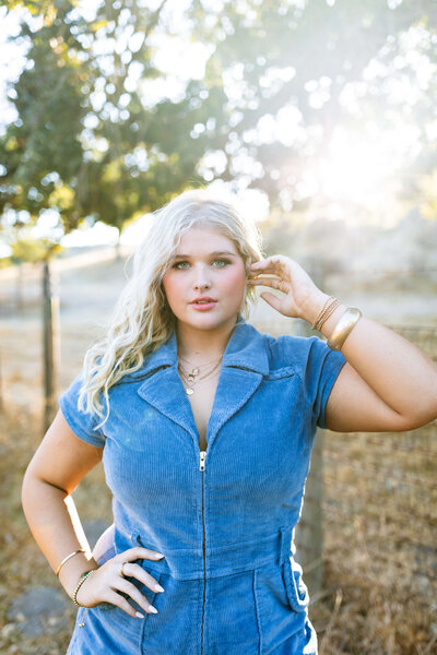 blonde girl wearing gold jewelry and blue jumpsuit on a ranch